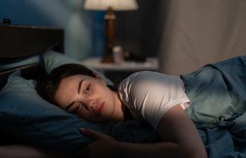 Young sad woman lying in bed late at night trying to sleep suffering insomnia. Girl in bed scared on nightmares looking worried and stressed. Sleeping disorder and insomnia concept