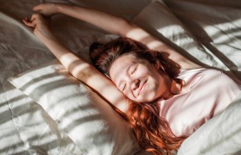Good morning, new day, weekend, holiday. Happy Young Woman sets on Bed, teen Girl Stretching arms after sleep and enjoying morning in cozy comfort bedroom interior