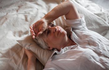 Unhappy elderly woman lying in bed at home thinking pondering over life problems, mourning or yearning, upset sad senior female relax in bedroom feel unwell or stressed suffering from insomnia